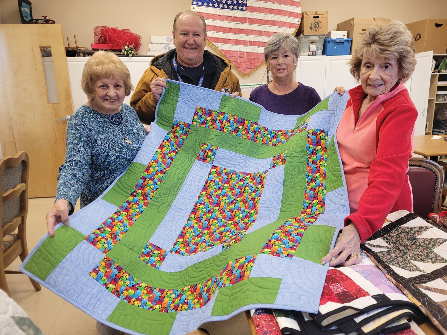 LIKE PATCHWORK: Members of the Giving Quilt Group at the Johnston Senior Center, from left to right, Marie Lanzi, Fran Zanni and Betty Bryda, check out a quilt they plan to send with John Reis (second from left), a caseworker with Children’s Friend and Services’ Project Connect.